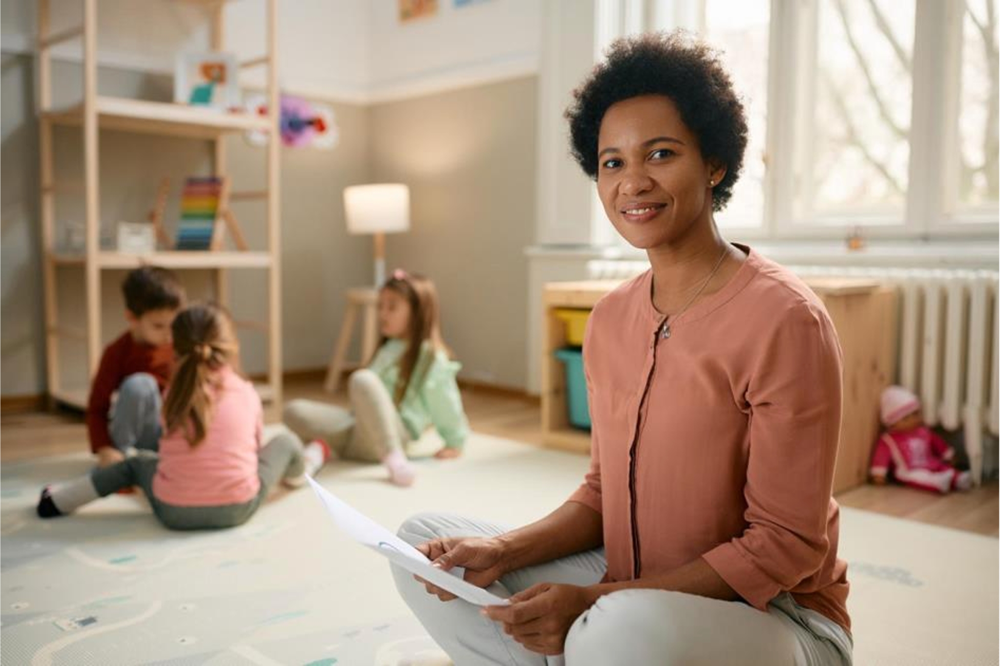 A woman sits on the floor with children appearing in the background