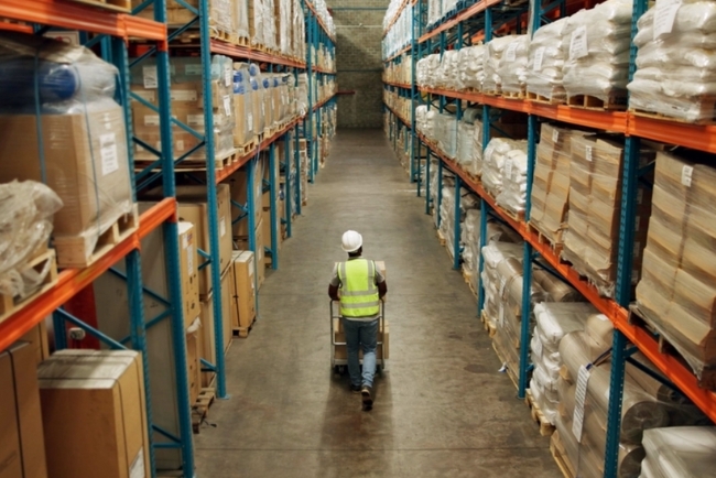 A person in a safety vest walks in an aisle in a warehouse