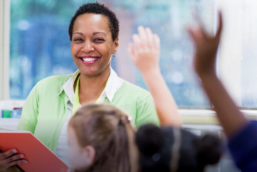 A teacher looks on as students raise their hands