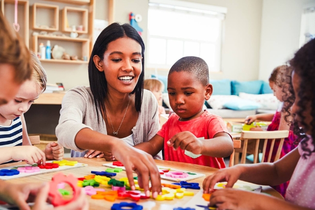 An adult woman sits with young children around a table playing with puzzles