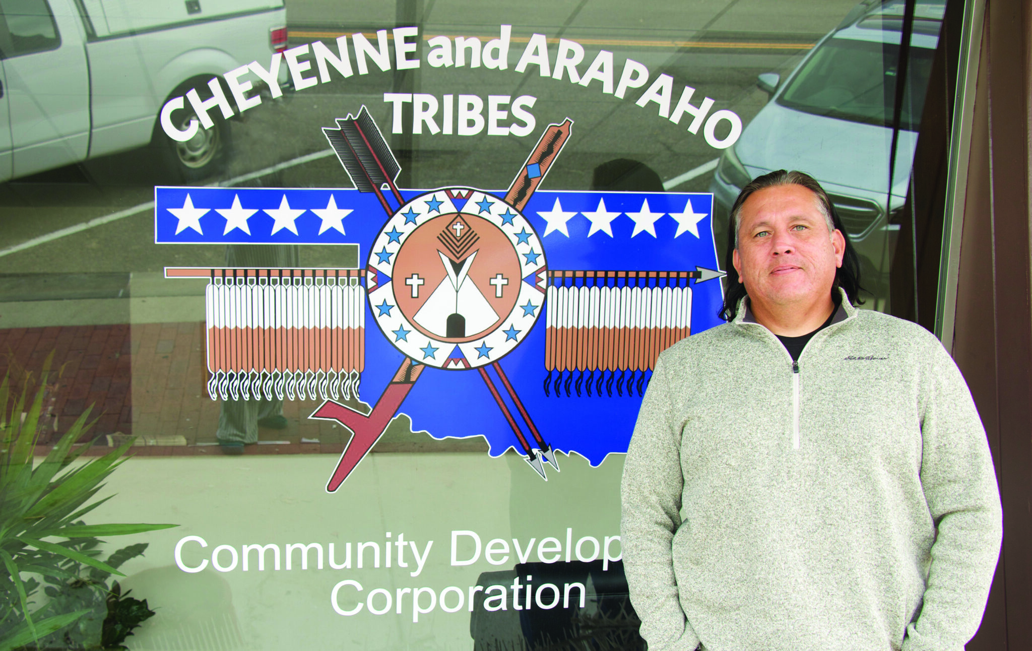 A man stands in front of a window that says "Cheyenne and Arapaho Tribes"