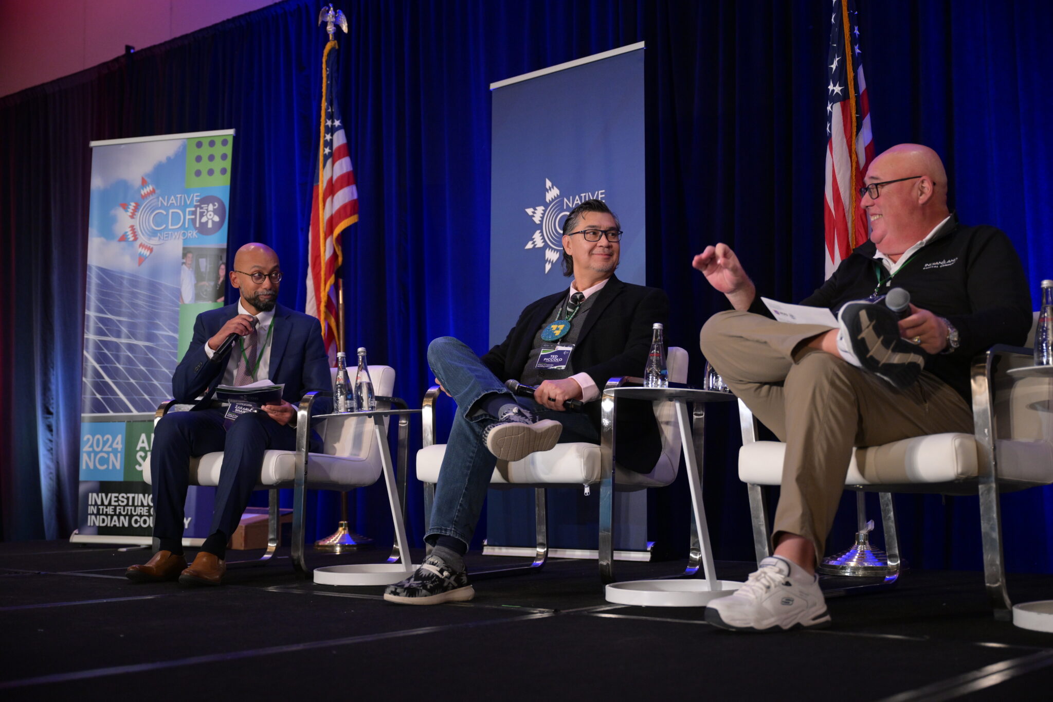 Three men speak and smile from a stage